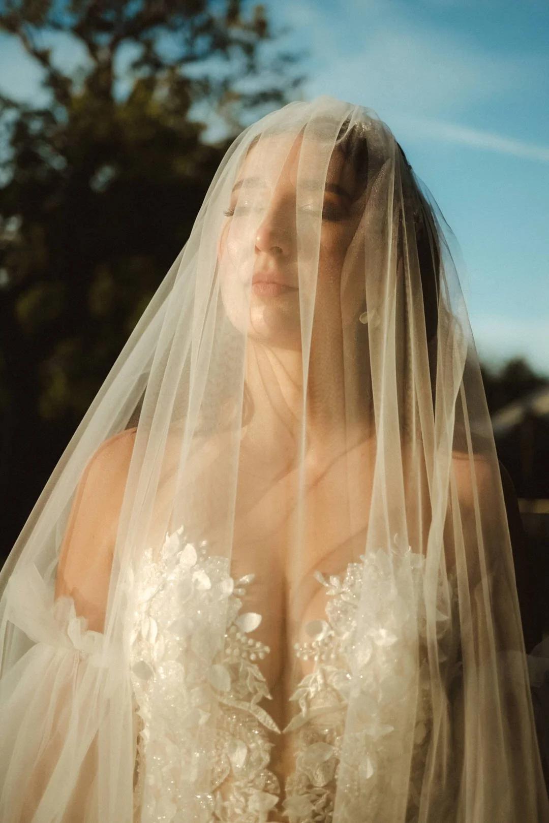 Braut mit Schleier über dem Gesicht und geschlossenen Augen im warmen Sonnenlicht