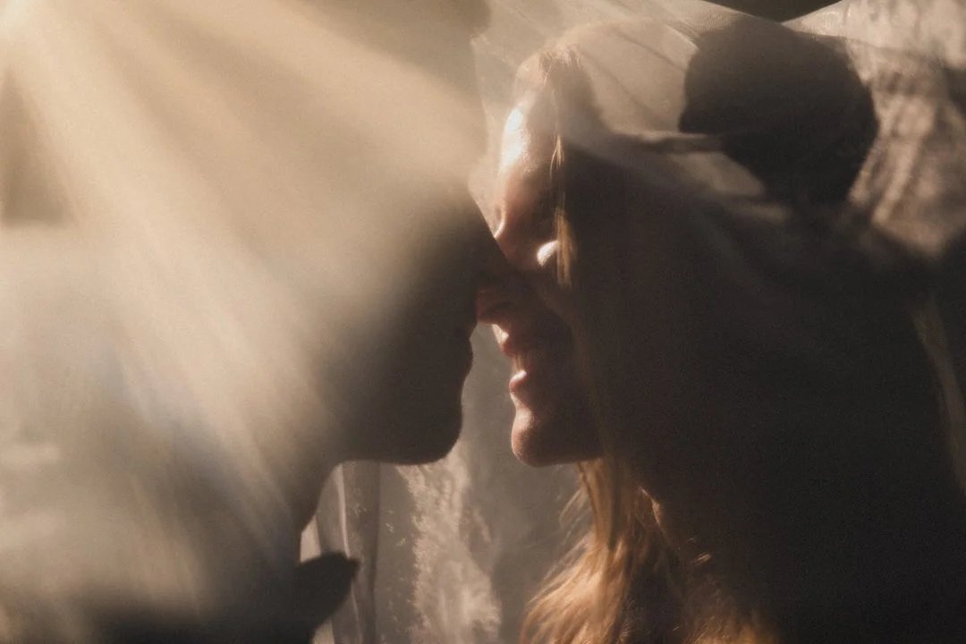 Brautpaar Stirn an Stirn im dramatischen Lichtspiel des Schleiers